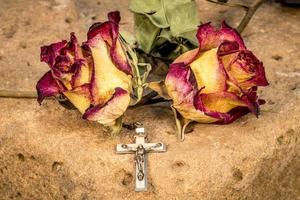 croix chrétienne sur chapelet et roses rouges jaunes sèches