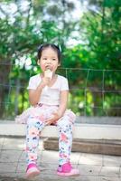 petite fille asiatique mangeant une glace à l'extérieur avec un arrière-plan flou de lumière naturelle photo