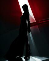 une femme dans une noir robe permanent dans de face de une rouge lumière photo
