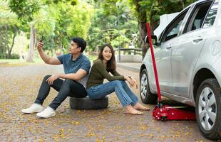 asiatique couple en utilisant téléphone intelligent pour assistance après une voiture panne sur rue. concept de véhicule moteur problème ou accident et urgence Aidez-moi de professionnel mécanicien photo