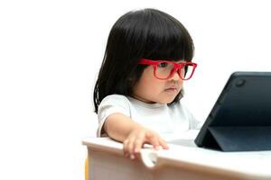 petite fille asiatique d'âge préscolaire portant des lunettes rouges et utilisant un tablet pc sur fond blanc, fille asiatique parlant et apprenant avec un appel vidéo avec une tablette, concept éducatif pour les écoliers. photo