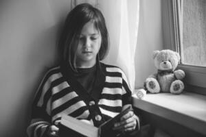 adolescent fille en train de lire une livre à Accueil par le fenêtre photo