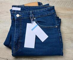 bleu jeans sur une en bois surface. le un pantalon sont soigneusement plié, et là est une marron cuir pièce à le taille de le jeans. photo