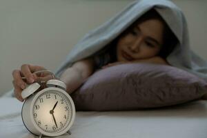 asiatique femme dans lit en retard en essayant à sommeil Souffrance insomnie, sans sommeil ou effrayé dans une cauchemar, à la recherche triste inquiet et stressé. fatigué et mal de crâne ou migraine veille en haut dans le milieu de le nuit. photo