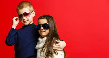 marrant charmant les enfants. à la mode peu garçon et fille dans lunettes, jeans, blanc chemises élégant des gamins dans décontractée vêtements dans choqué. mode les enfants photo