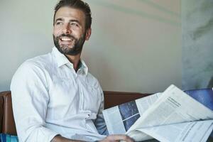 portrait de content homme d'affaire portant blanc chemise séance sur canapé avec journal photo