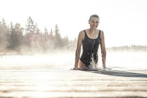 content femme portant noir maillot de bain baignade dans une Lac à Matin brouillard photo