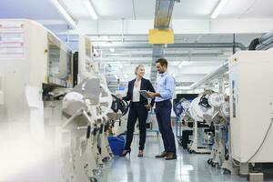 Masculin technicien en portant numérique tablette tandis que discuter avec femme d'affaires permanent par machinerie à usine photo