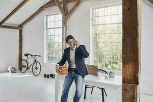 souriant homme d'affaire avec basketball sur cellule téléphone dans attique photo
