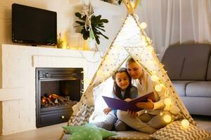 famille mère en train de lire à les enfants livre dans tente à Accueil photo