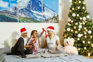 famille dans Noël chapeau, bébé mère et père, Trois les personnes à la recherche à caméra sur blanc Contexte photo