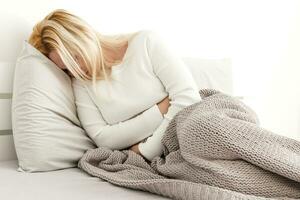 Jeune femme Souffrance de abdominal douleur tandis que séance sur lit à Accueil photo