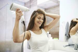 portrait de en riant femme en utilisant cheveux séchoir dans le salle de bains photo