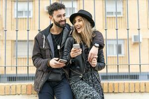 portrait de en riant Jeune couple avec leur mobile Téléphone (s dans le ville photo