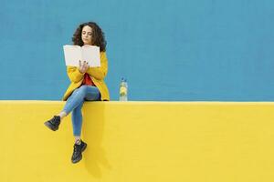 Jeune femme séance sur Jaune mur en train de lire une livre photo