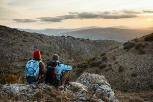 Masculin et femelle randonneurs profiter le coucher du soleil tandis que séance sur Roche Montagne pendant vacances photo