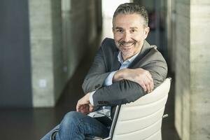 portrait de une souriant mature homme d'affaire séance sur chaise dans Bureau photo