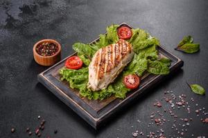 morceaux de poulet, tomates et feuilles de laitue sur fond de béton foncé photo