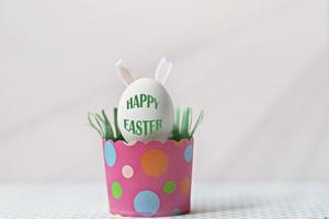 œuf de poule blanc avec oreilles de lapin dans un bac en papier rose écologique, boîte. concept de joyeuses fêtes de pâques. texte anglais joyeuses pâques photo