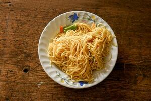 gros plan et vue de dessus nouilles chinoises frites dans une assiette en céramique blanche sur fond de bois. les thaïlandais et les chinois mangent des aliments végétaliens populaires au festival végétarien chinois en octobre chaque année photo