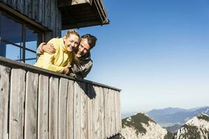 couple penché sur balcon de une Montagne cabane, avec bras autour photo