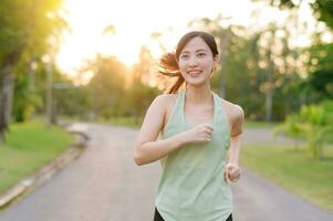 en forme asiatique Jeune femme le jogging dans parc souriant content fonctionnement et profiter une en bonne santé Extérieur mode de vie. femelle joggeur. aptitude coureur fille dans Publique parc. en bonne santé mode de vie et bien-être étant concept photo