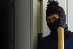 voleur masqué avec batte de baseball se cachant derrière la porte photo