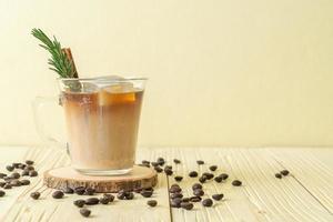 verser du lait dans un verre à café noir avec glaçon, cannelle et romarin sur fond de bois photo