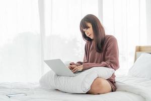 femme asiatique travaillant avec un ordinateur portable sur le lit à la maison photo