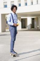homme d'affaires noir sur une planche à roulettes tenant un smartphone à l'extérieur. photo