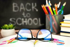 vacances concept pour enseignants journée. lunettes, école Provisions et une tableau noir dans le Contexte avec le mots retour à école. fermer. sélectif se concentrer. photo