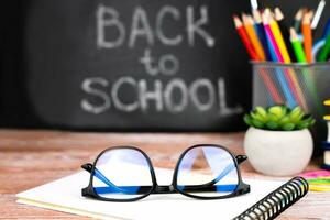 lunettes, école Provisions et une tableau noir dans le Contexte avec le mots retour à école. fermer. sélectif se concentrer. photo