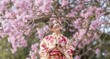 Japonais femme dans traditionnel kimono robe en portant sucré hanami dango dessert tandis que en marchant dans le parc à Cerise fleur arbre pendant printemps Sakura Festival photo