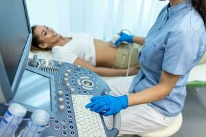 côté vue portraits de gynécologue dans stérile gants en utilisant ultrason scanner tandis que examiner femelle patient. femme mensonge sur lit de repos sur flou Contexte photo