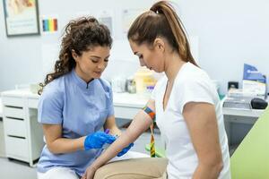 préparation pour du sang tester avec jolie Jeune femme par femelle médecin médical uniforme sur le table dans blanc brillant chambre. infirmière perce le les patients bras veine avec aiguille Vide tube. photo