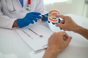 le dentiste détient une dentier dans le sien main et spectacles le patient le position de le problème dent et le dentiste explique Comment à traiter le dent pour le patient à comprendre. copie espace pour texte photo