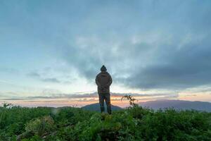 Masculin touristes supporter sur Haut de une Montagne dans le Matin à la recherche à le magnifique vue de le crépuscule comme le Soleil monte sur le horizon et prier à Dieu pour bénédictions selon à le Christian foi. photo