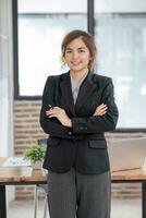 portrait, Jeune sur de soi souriant asiatique affaires femme portant costume permanent dans Bureau avec bras franchi. photo