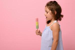 en bonne santé végétalien la glace crème popsicle dans main de une 4 ans jolie bébé fille avec rose mur à Contexte avec copie espace . été dessert et de bonne humeur été ambiance concept photo