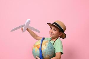 adorable enfant garçon pièces avec une papier avion simuler une vol autour le planète Terre. concepts à propos voyage, tourisme, la géographie et aviation. rose Contexte avec copie espace photo