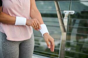 fermer de athlète femme dans rose T-shirt en mettant sur blanc athlétique éponge bracelets avoir prêt pour Matin faire du jogging en train de préparer à courir pour conscience marathon. actif mode de vie, santé, corps se soucier concept photo