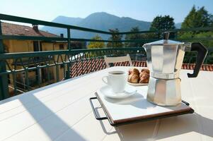 italien percolateur et une tasse de fraîchement brassée café sur une table sur le balcon contre le toile de fond de le montagnes photo