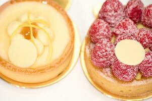 fermer. aérien vue de français desserts - une citron et framboise Meringue gâteau et tartelette sur une blanc plaque. photo