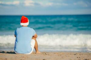 jeune homme en bonnet de noel pendant les vacances à la plage de noël photo