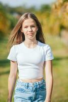 une fille dans une blanc chemise et bleu jeans permanent suivant à une paume arbre photo