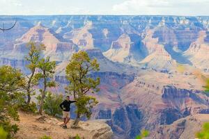 Jeune promeneur est permanent sur une raide falaise prise dans le incroyable vue plus de célèbre grandiose canyon sur une magnifique ensoleillé journée avec bleu ciel dans été, grandiose canyon nationale parc, Arizona, Etats-Unis photo