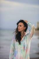 Jeune content femme sur le plage prendre plaisir sa été vacances. femme en marchant le long de le mer dans soir. photo