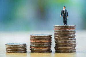 Close up miniature businessman standing on money stack coin