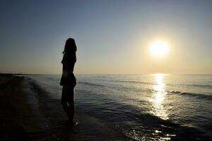 silhouette de une fille contre le le coucher du soleil par le mer photo