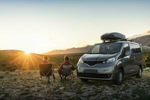 homme et femme séance près campeur van, à la recherche à paysage à le coucher du soleil photo